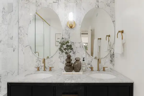 Black double vanity with oval mirrors and marble tile