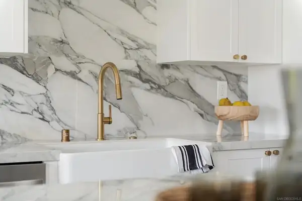 Brass faucet and farmhouse sink against marble backsplash